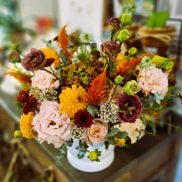 Mixed bouquet in a white vase with peach, yellow, and burgundy flowers