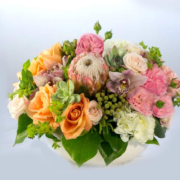 Mixed bouquet of peach, pink, and white flowers in a low white container
