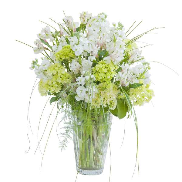 Tall arrangement of white and green flowers with wispy grass in a clear glass vase