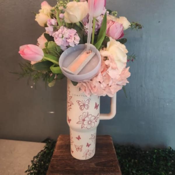 Pastel pink and white flower arrangement in a printed travel tumbler with a small candle on a wooden stand