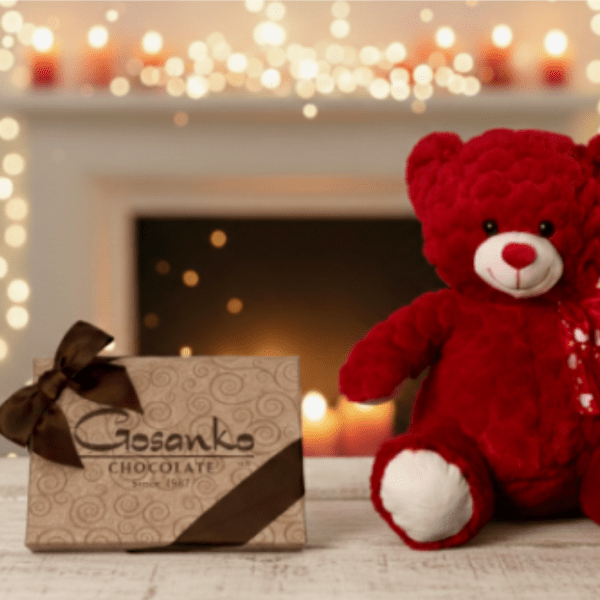 Red teddy bear and decorative chocolate box on a wooden surface with soft candlelight in the background.