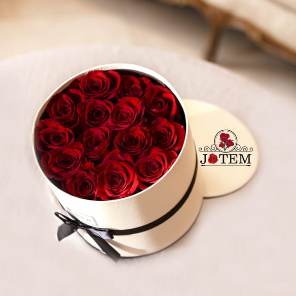 Round box filled with red roses and tied with a black ribbon