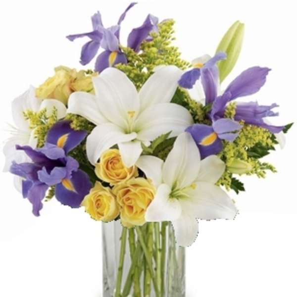 Mixed bouquet of white lilies, yellow roses, and purple irises in a clear glass vase