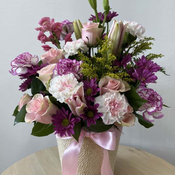Pink and purple mixed bouquet in a woven basket with a pink ribbon