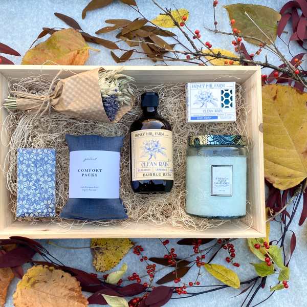 Wooden gift box with dried bouquet, candle, soaps, bubble bath, and comfort pack on autumn leaves