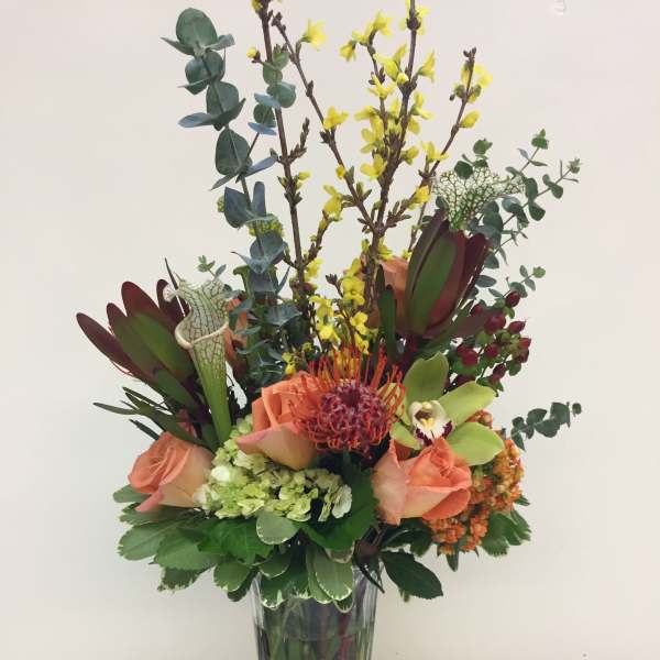 Tall mixed bouquet in a clear glass vase with peach roses and yellow blooms