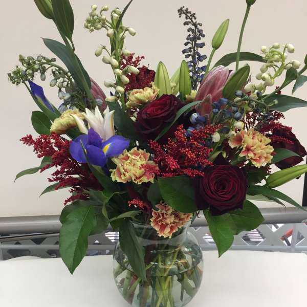 Mixed bouquet of roses, lilies, and irises in a glass vase