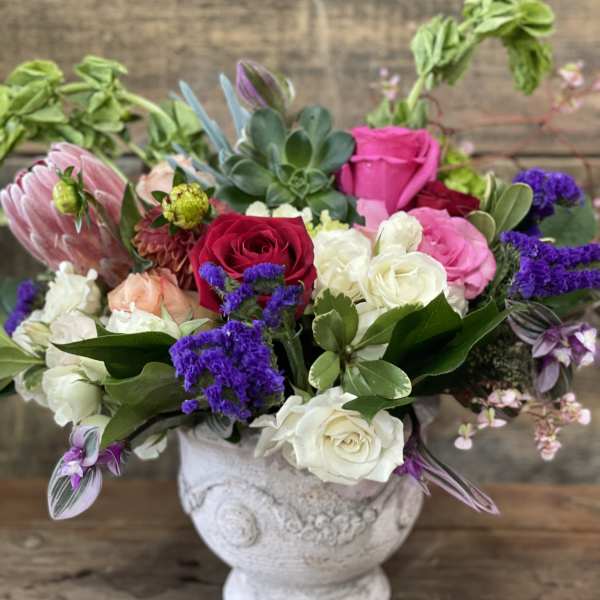 Mixed bouquet of roses and purple blooms in a white vase