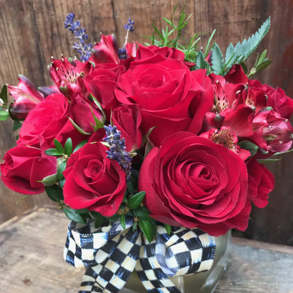 Red roses and alstroemeria in a square glass vase with a checkered ribbon