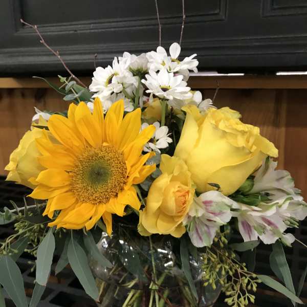 Yellow roses and a sunflower in a glass vase with white daisies