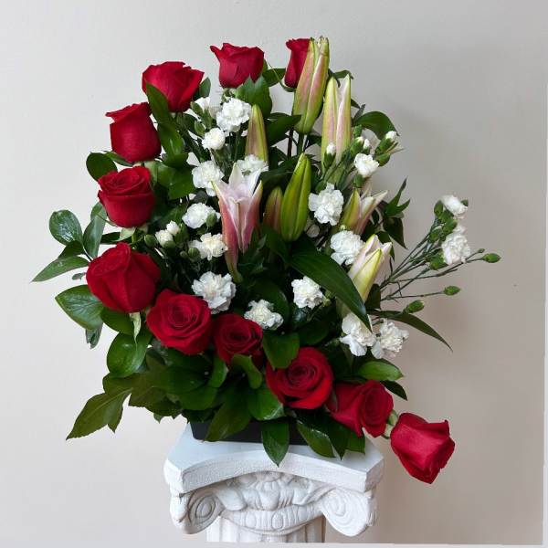 Red roses and white lilies arranged in a vase with small white filler flowers