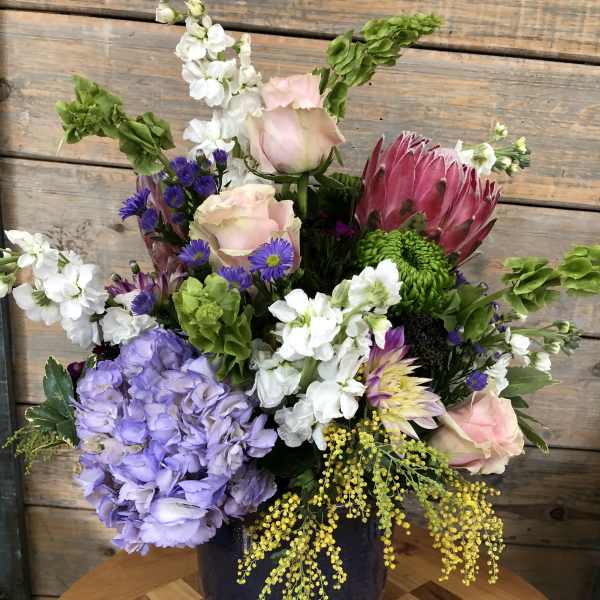 Mixed bouquet with pink roses, purple hydrangea, and a large pink protea in a vase