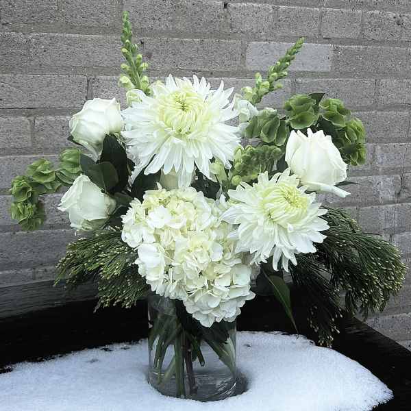 White floral arrangement in a clear glass vase with green accents