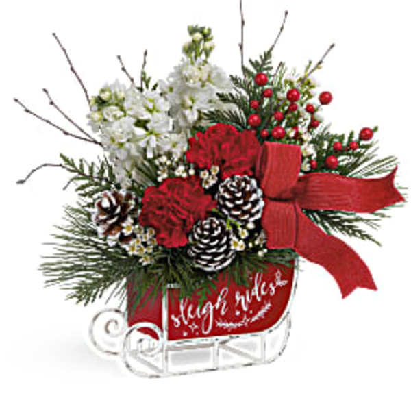 Holiday floral arrangement with red carnations, white blooms, pinecones, and a red bow in a sleigh