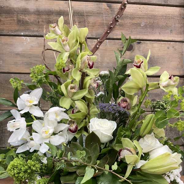 Mixed floral arrangement with white and green orchids and roses in a low container