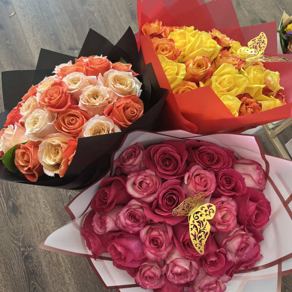 Three rose bouquets in pink, yellow, and peach tones wrapped in colored paper