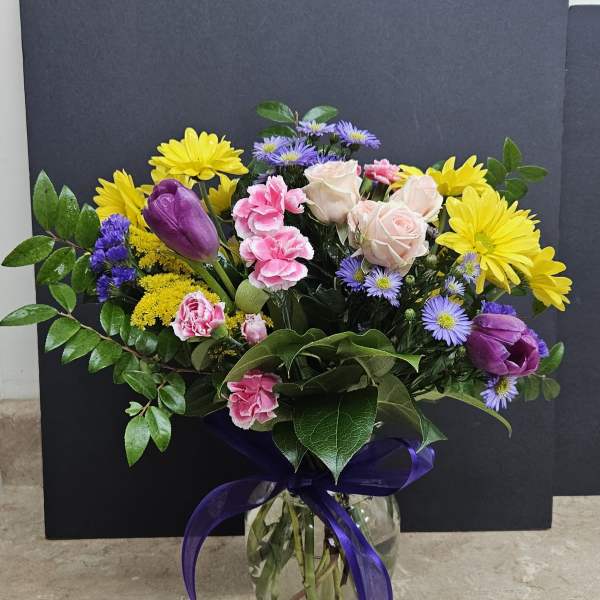 Mixed bouquet of yellow daisies, pink roses, and purple tulips in a glass vase