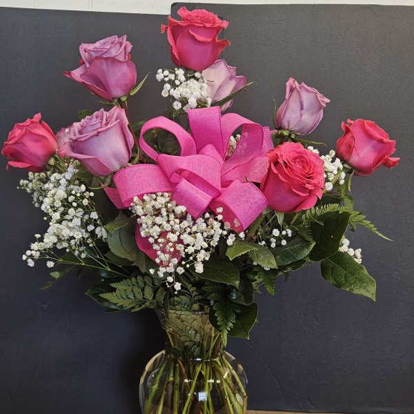 Pink and lavender roses in a glass vase with a bright pink ribbon