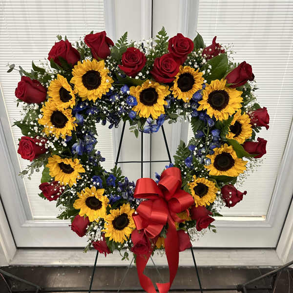 Heart-shaped wreath of red roses and sunflowers with a red bow