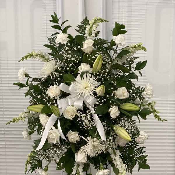 White floral standing spray with lilies, roses, and ribbon on an easel