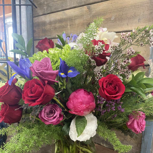 Mixed bouquet of roses, iris, and peonies in a clear glass vase