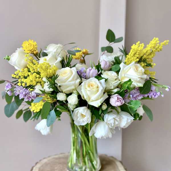 Bouquet of white roses and yellow filler flowers in a glass vase