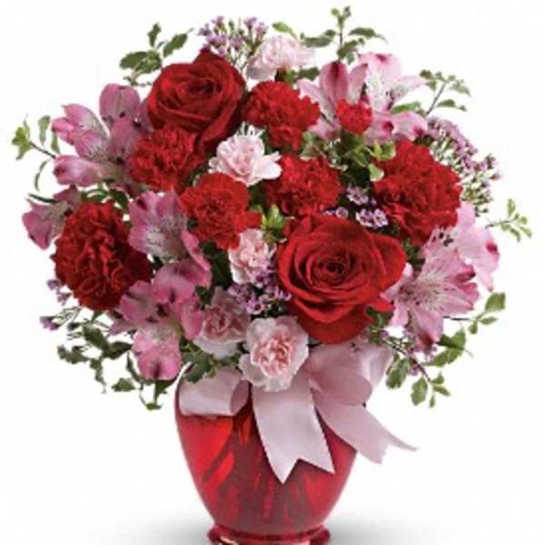 Red and pink flower bouquet in a red vase with a ribbon