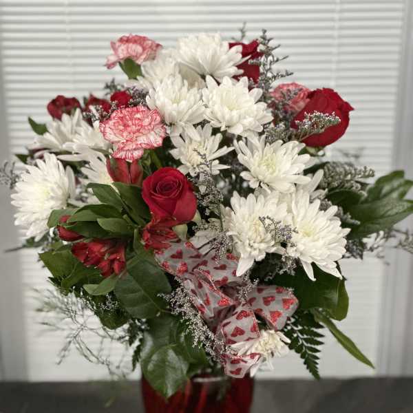 Red roses and white daisies in a red vase with heart ribbon