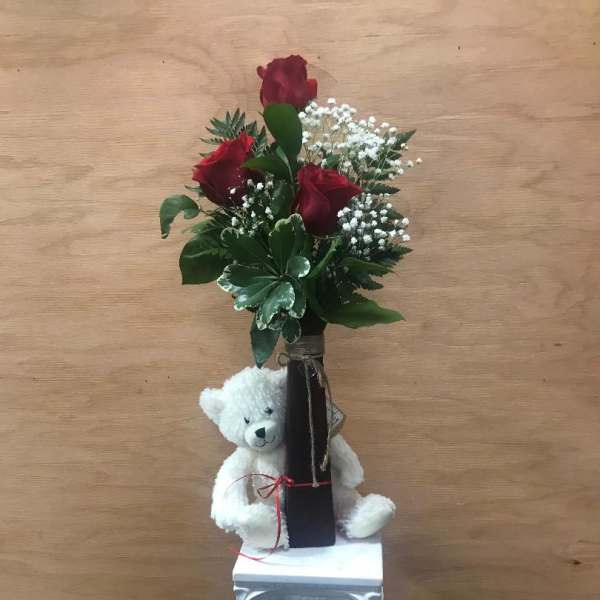 Red roses in a tall vase with a white teddy bear