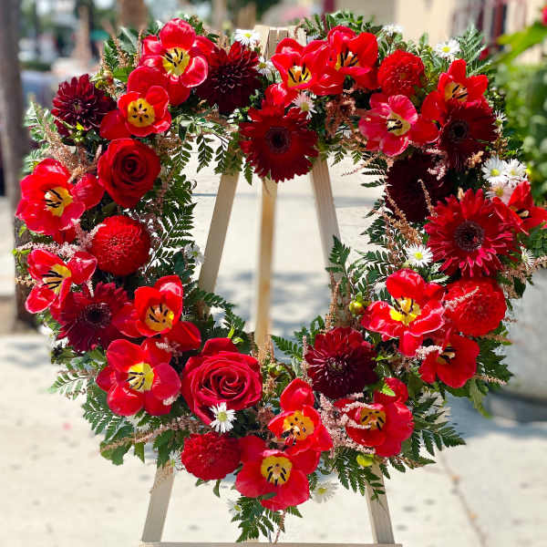 Heart-shaped floral wreath with red tulips and roses on a wooden stand