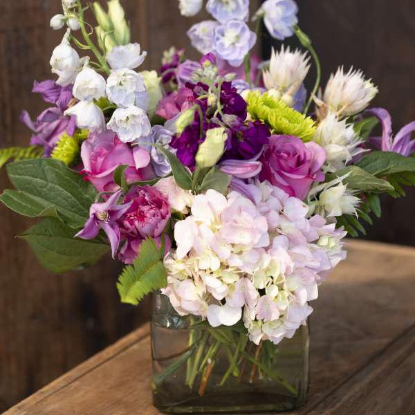 Mixed pink, purple, and white flowers in a square glass vase