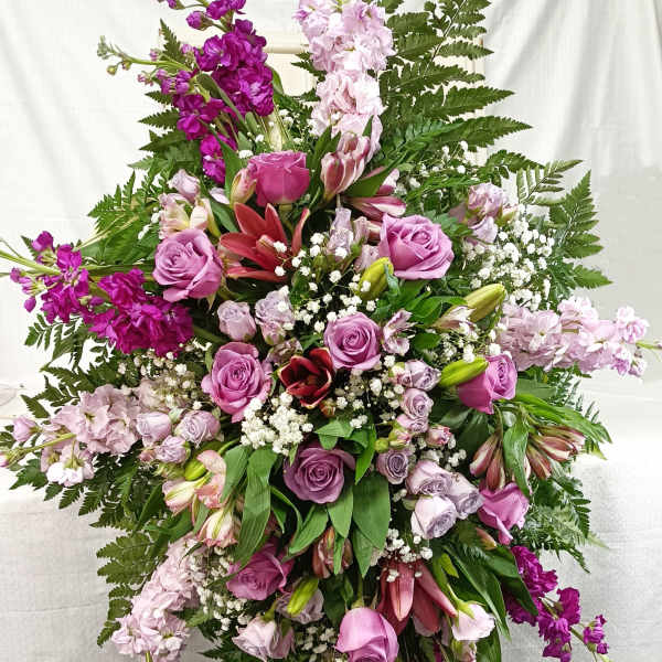 Tall cascading arrangement of purple roses, pink lilies, and white filler flowers in an oval spray shape.