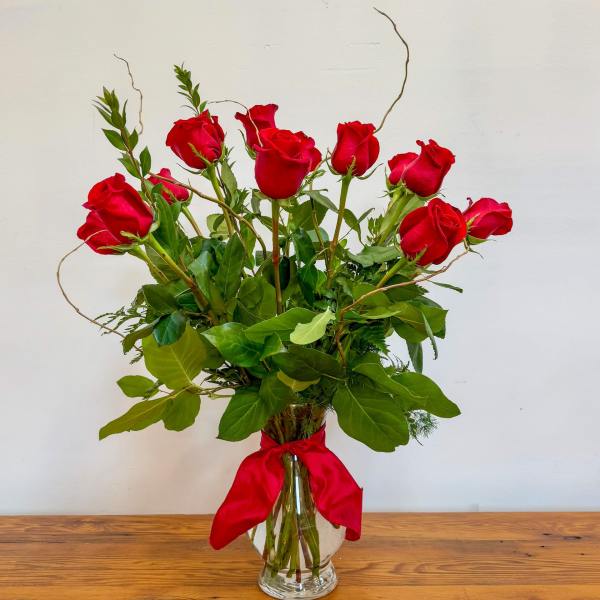 Tall arrangement of red roses in a clear glass vase with a red ribbon bow