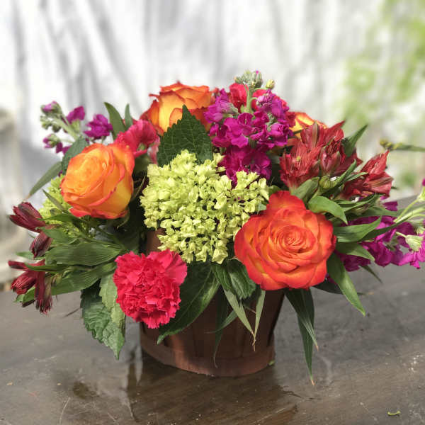 Bright mixed arrangement with orange roses, green hydrangea, and pink blooms in a small wooden container