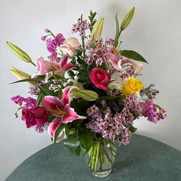 Mixed bouquet of lilies, roses, and small pink flowers in a glass vase