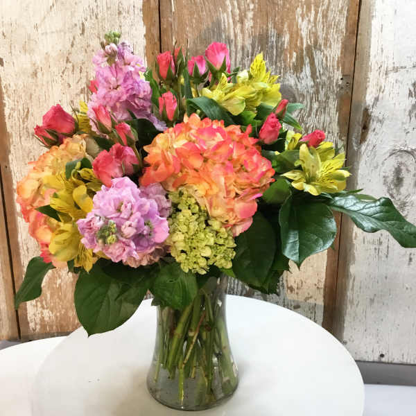 Mixed bouquet of pink, orange, and yellow flowers in a glass vase