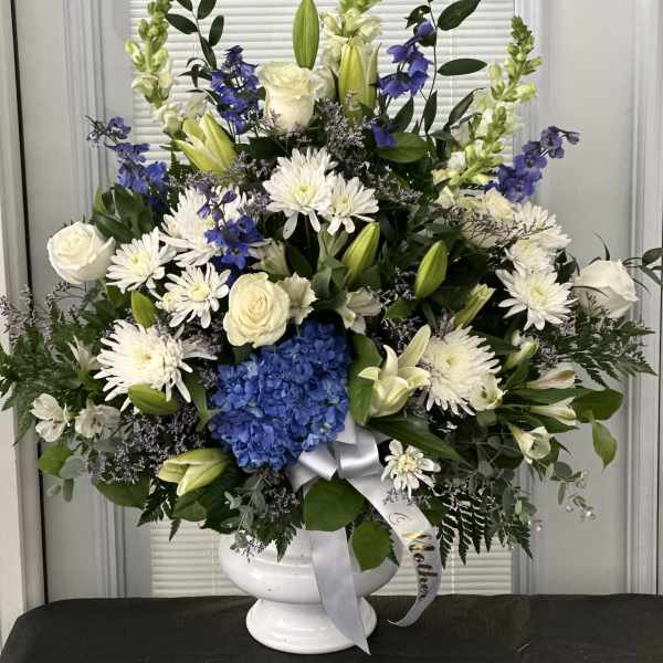 Large white and blue floral arrangement in a white urn vase