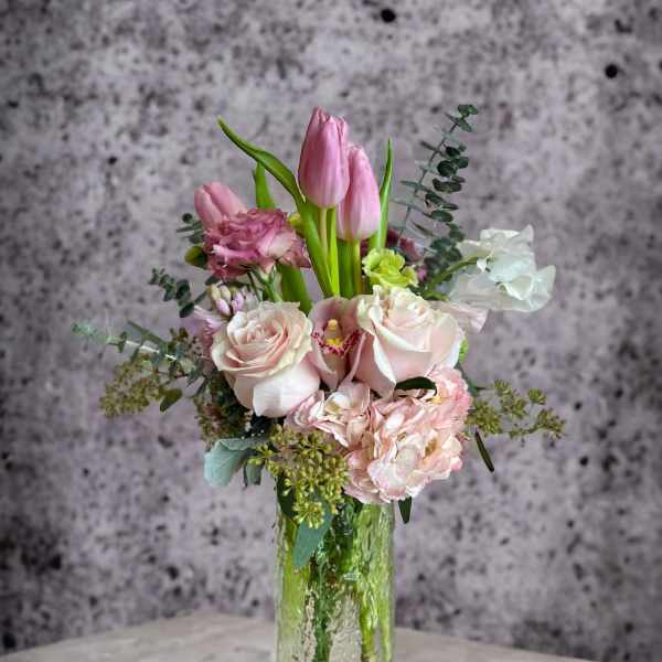 Pink tulips and pale roses arranged in a clear glass vase