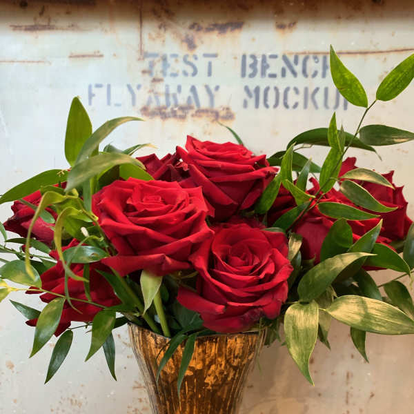 Red roses arranged in a gold vase with green foliage