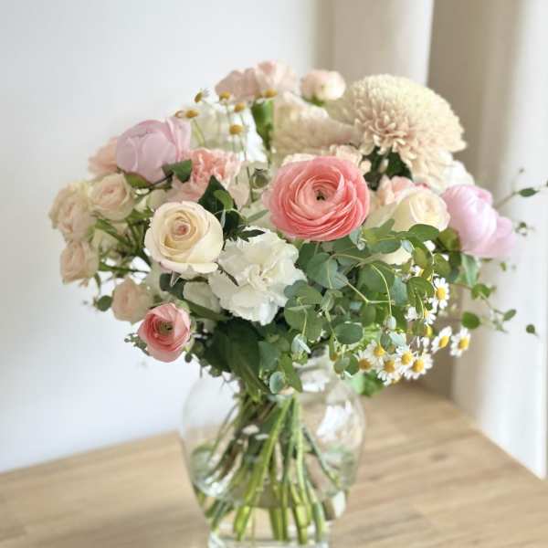 Pastel bouquet of roses, ranunculus, and white blooms in a clear glass vase