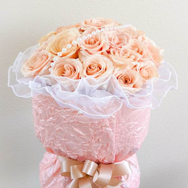 Peach roses arranged in a pink wrapped bouquet with a ribbon and pearl accents