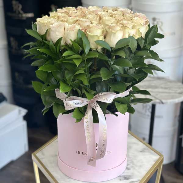 Cream roses arranged in a pink hat box with a ribbon