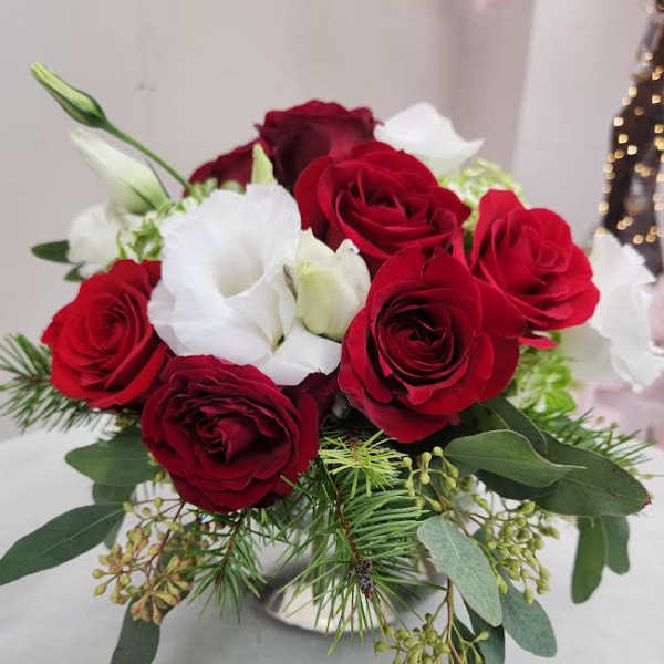 Low arrangement of red roses and white lisianthus with holiday greenery in a silver vase