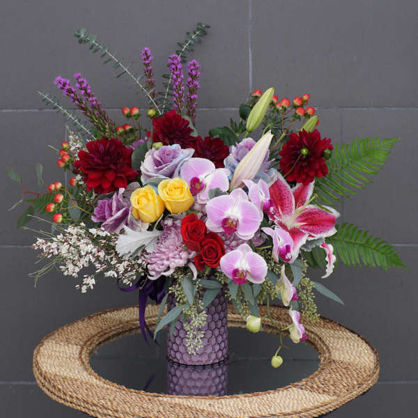 Mixed bouquet in a purple vase with orchids, lilies, roses, and dahlias