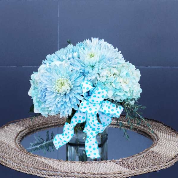 Blue and white flower arrangement in a glass vase with a polka-dot ribbon
