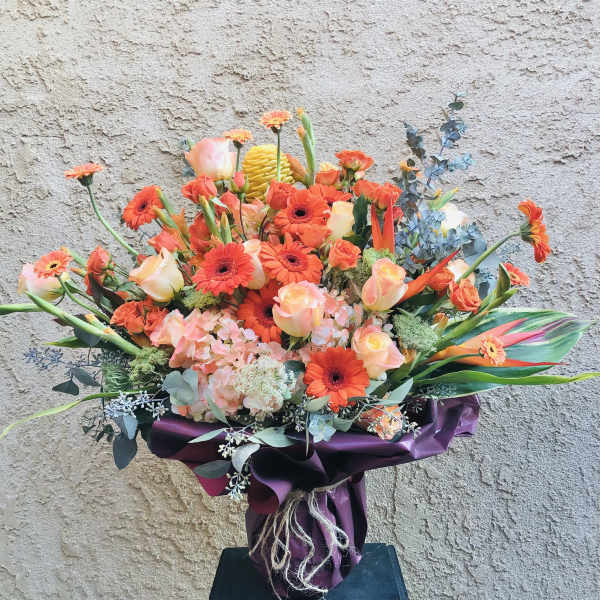 Orange and peach bouquet with gerbera daisies and roses in purple wrap
