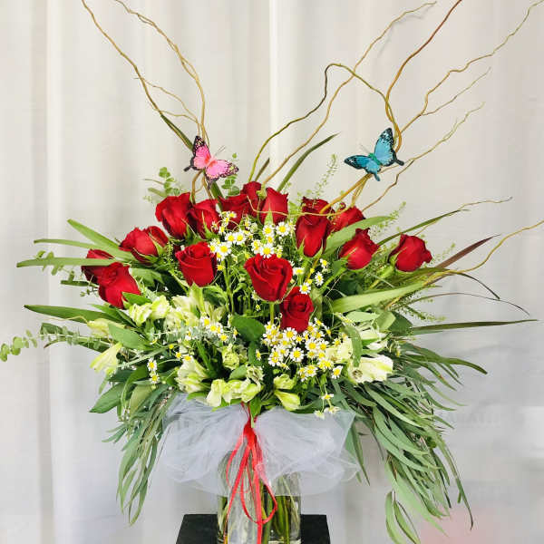 Tall bouquet of red roses and white flowers in a glass vase with butterfly picks