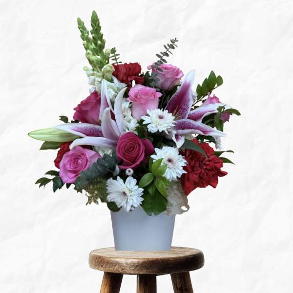 Mixed bouquet of pink roses, lilies, and white daisies in a blue vase