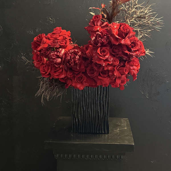 Red rose arrangement in a black vase with dark foliage