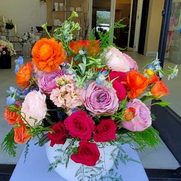 Colorful arrangement of roses and ranunculus in a white bowl-shaped vase